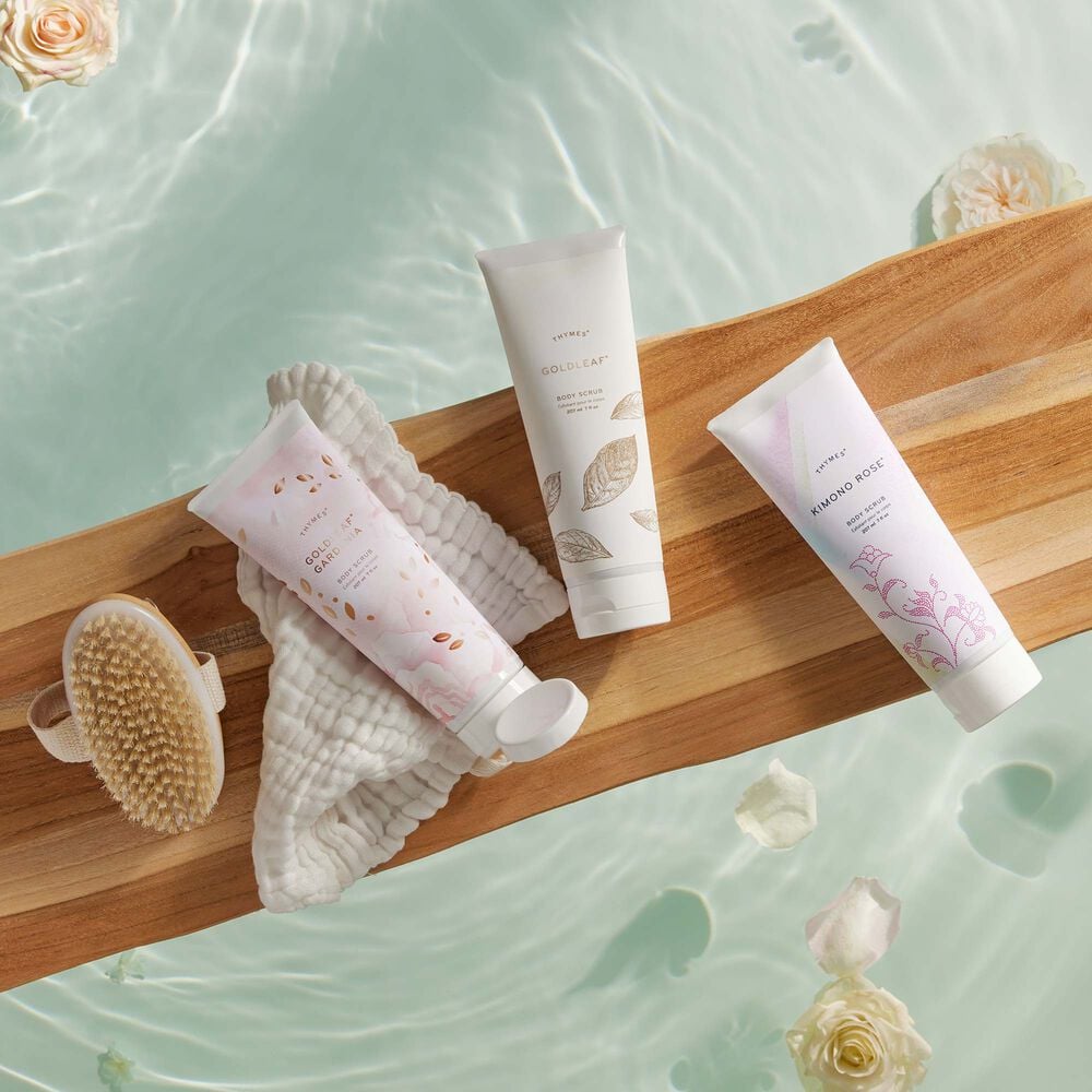 Thymes Kimono Rose Body Scrub for exfoliation laying next to other Thymes Body Scrubs on wooden bath tray in bath tub image number 2